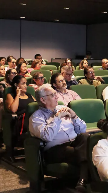 Asistentes sentados en las butacas verdes del auditorio, siguiendo la presentación con atención.