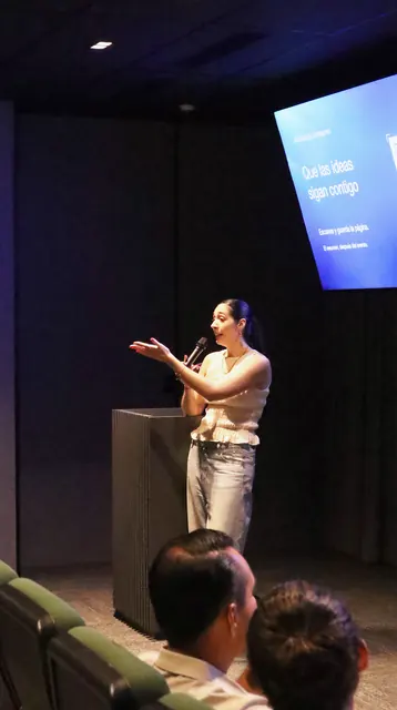 Andrea Molina Montalvo en el pódium, explicando con las manos, con la pantalla de la presentación encendida detrás.